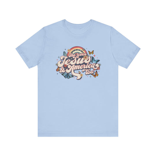 A light blue She Loves Jesus and America Tee, featuring butterflies and flowers graphic design. Unisex jersey tee made of 100% cotton, with ribbed knit collars and tear away label. Sizes XS to 3XL.