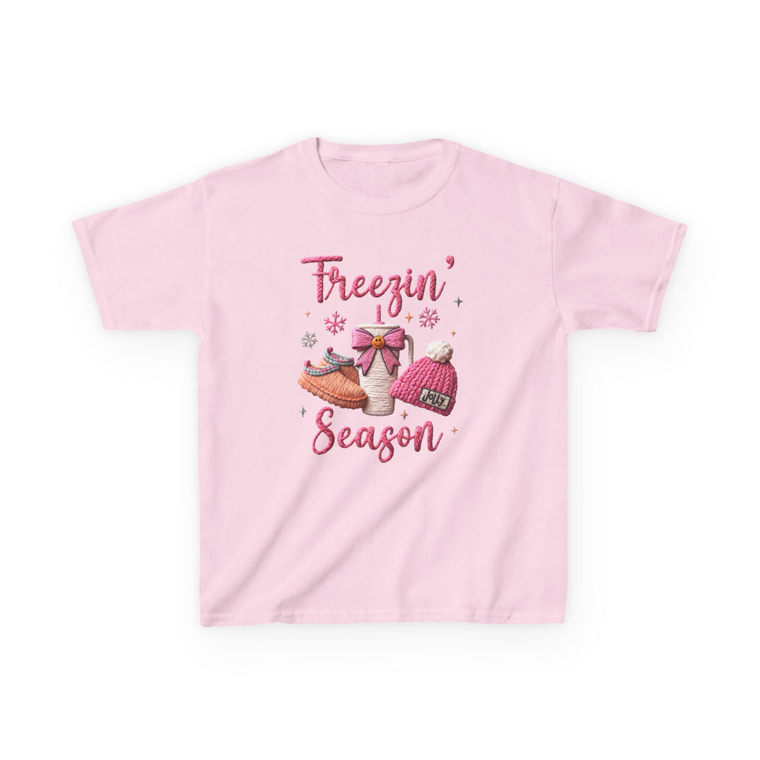 Freezin Season Kids Tee featuring a winter-themed graphic with cozy elements like a mug, slippers, and beanie, on a light-pink, short-sleeve cotton shirt.