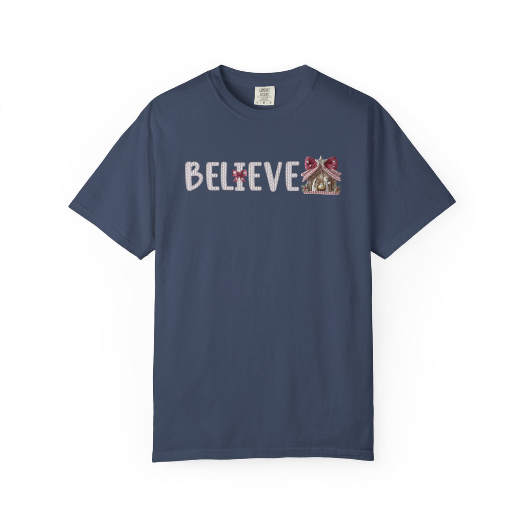 Believe Tee: Navy-blue short-sleeve t-shirt with “BELIEVE” in white rope-stitch, featuring a red bow and gingerbread house motif.