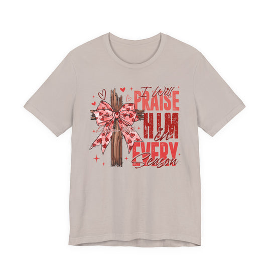 Praise in Every Season Heart Tee features a wooden cross with a pink bow, hearts, and sparkles, showcasing faith and Valentine's charm in a unisex cotton tee.
