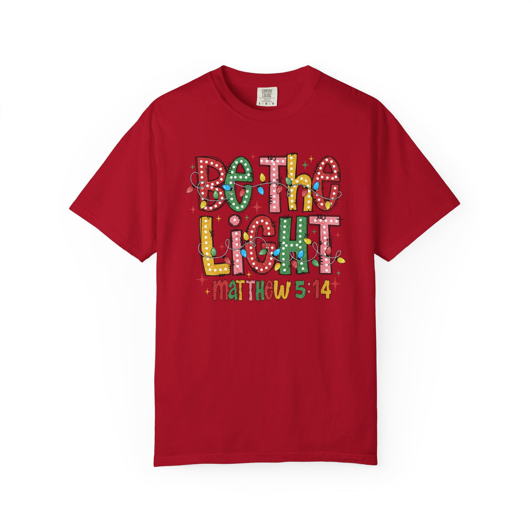 Red 'Be the Light' T-shirt featuring festive lettering and Bible verse Matthew 5:14, offering a comfortable, stylish fit from Faith Family Designs.