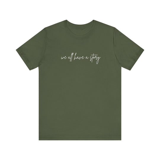 We all have a Story Tee, green with white text, featuring a classic unisex fit and soft cotton fabric, perfect for casual wear.