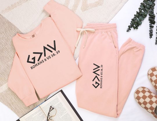 God is Greater Sweatpants feature pink fabric with black text, offering a vintage vibe. Made from ringspun cotton, they provide a relaxed fit and retro look.