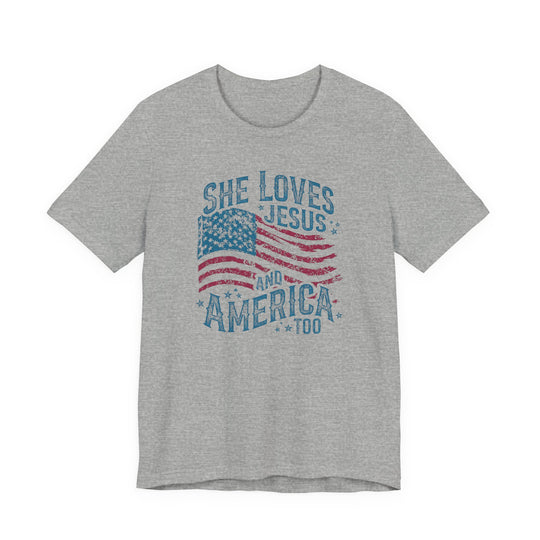 Heather-gray tee with vintage American flag graphic and She Loves Jesus And America Too text, showcasing a classic unisex fit for Faith Family Designs.