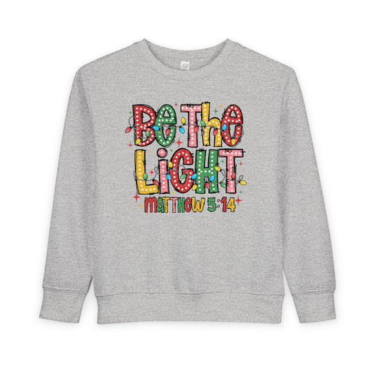 Light-gray toddler crewneck sweatshirt with Be the Light design, featuring colorful, polka-dotted letters wrapped in Christmas lights, highlighting comfort and durability.