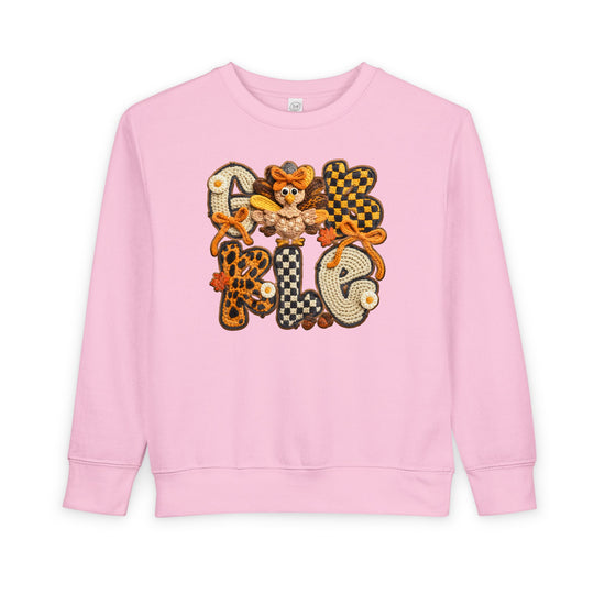 Light-pink Gobble toddler crewneck sweatshirt with crochet-style applique featuring colorful letters, bows, flowers, fall leaves, and a cute crochet turkey.
