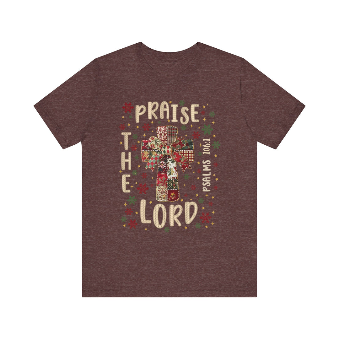 Praise the Lord Tee with quilt-patterned cross, festive bow, snowflakes, stars, and Psalms 106:1 text. Classic fit, soft cotton, suitable for all.