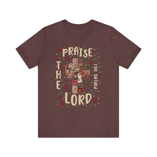 Praise the Lord Tee with quilt-patterned cross, festive bow, snowflakes, stars, and Psalms 106:1 text. Classic fit, soft cotton, suitable for all.
