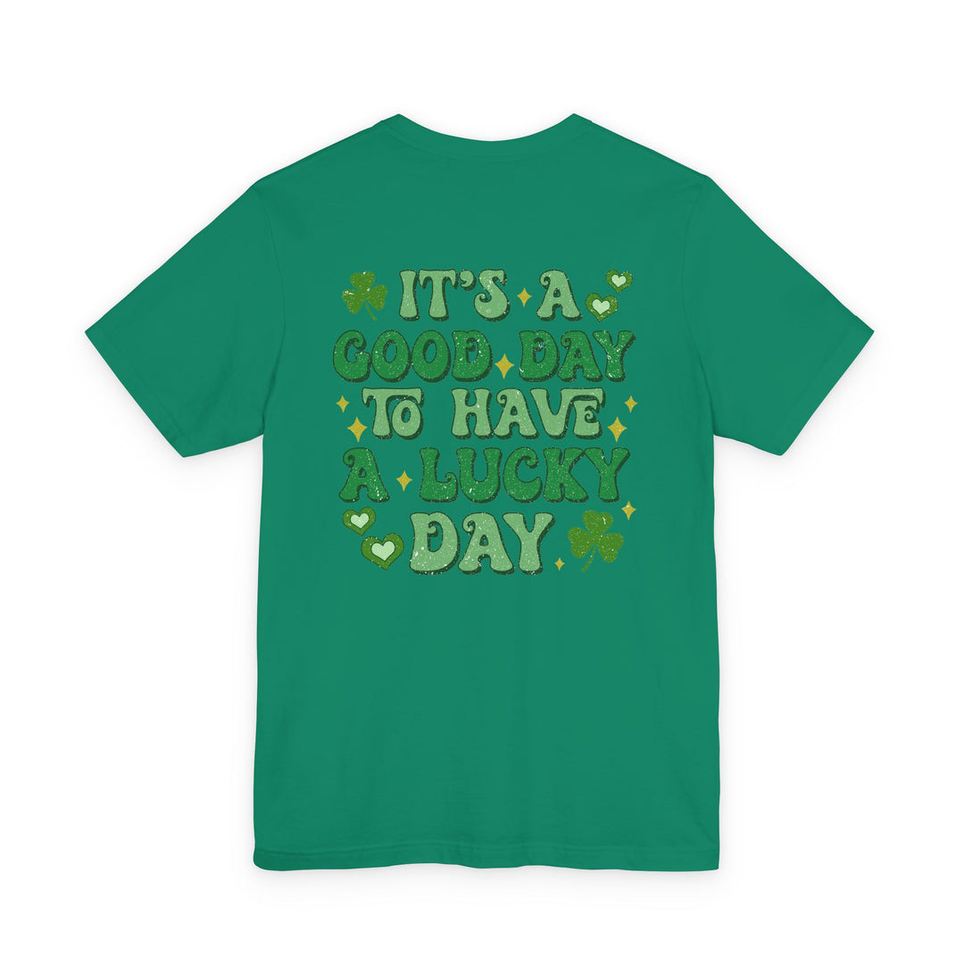 Good Day Lucky Day Tee features a retro-style graphic with clovers, hearts, and stars on a green background, embodying a playful St. Patrick’s Day theme.