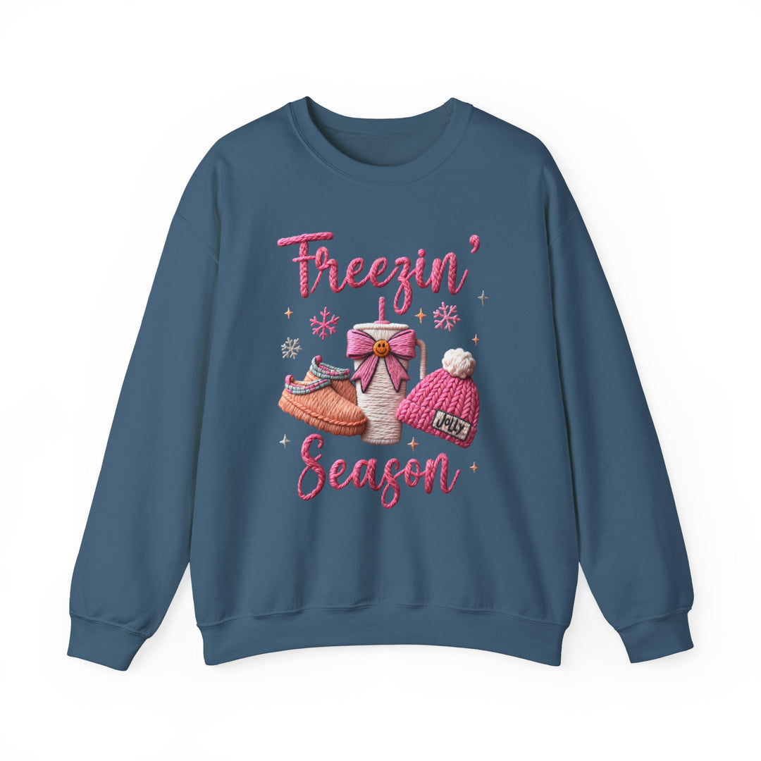 Freezin Season Crew sweatshirt with winter-themed graphic, featuring Freezin’ Season text, slippers, hot drink cup, knit beanie, snowflakes, and sparkles on a blue crewneck.