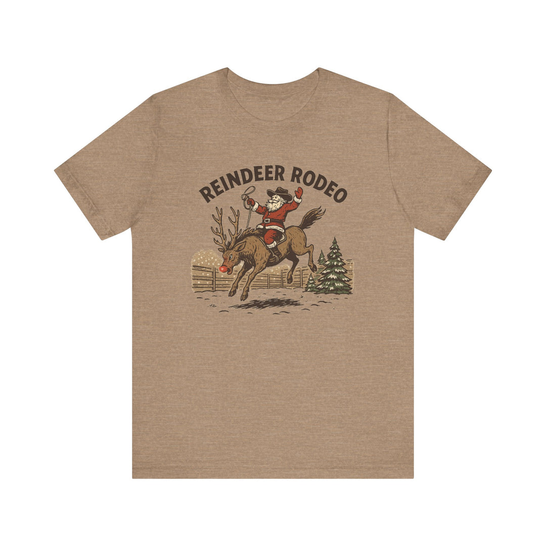 Reindeer Rodeo Tee: Santa in cowboy hat rides a reindeer, lasso in hand, amid snowflakes, on a soft, unisex, khaki-colored graphic T-shirt.