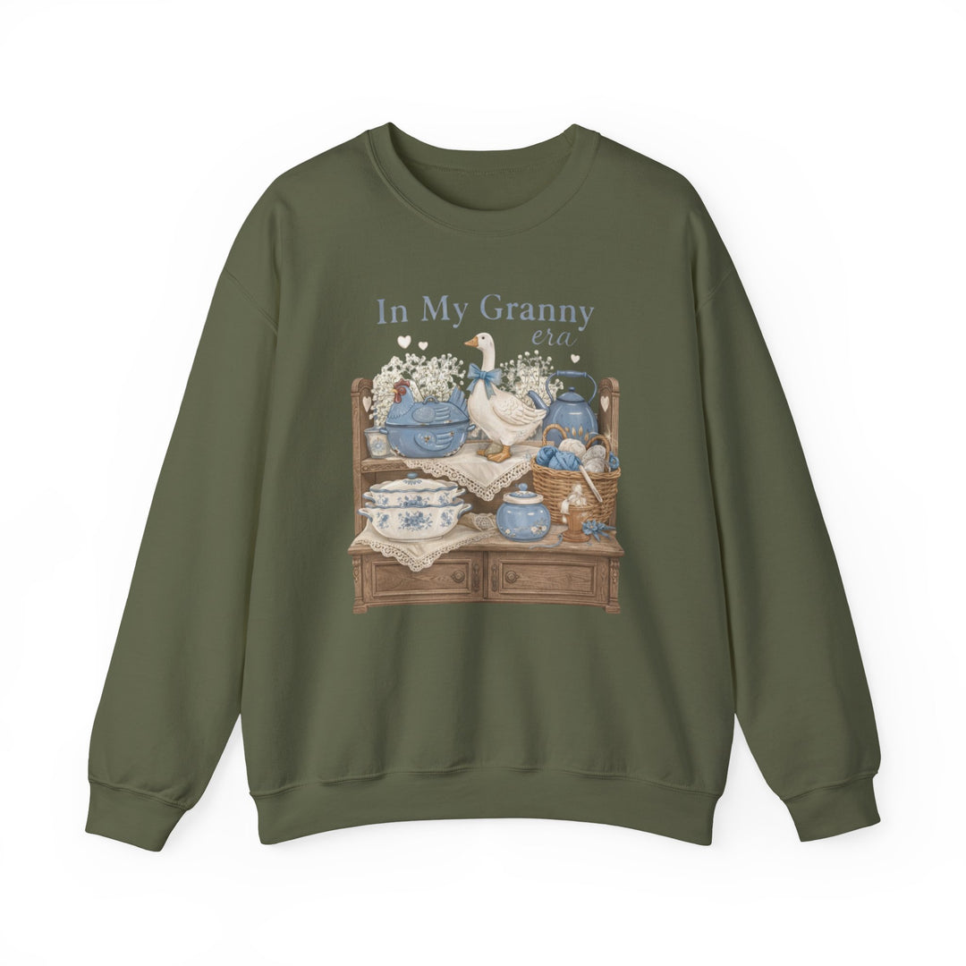 In My Granny Era Crew: Olive-green crewneck sweatshirt featuring a quaint sideboard illustration with china, yarn, and flowers, epitomizing cozy comfort and unique graphic design.