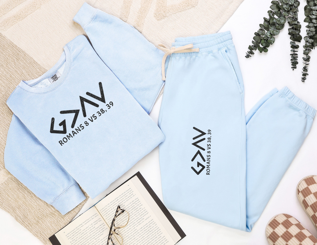 God is Greater Sweatpants, featuring a relaxed fit, made from 100% ring-spun cotton, displayed alongside a matching blue sweater on a blanket.