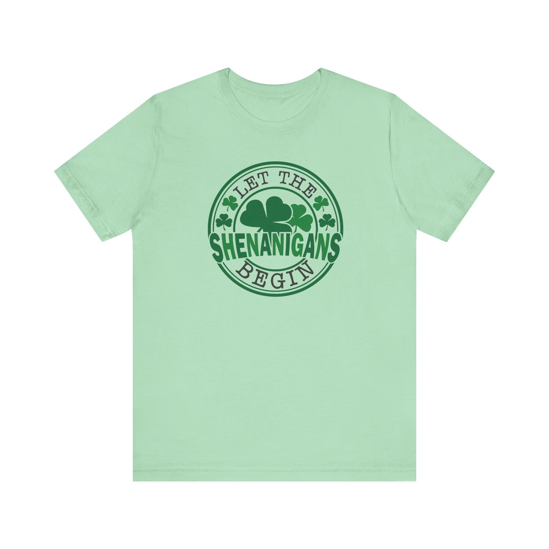 Let The Shenanigans Begin Tee features a green logo with four-leaf clovers, perfect for casual wear with ribbed knit collars and durable side seams.