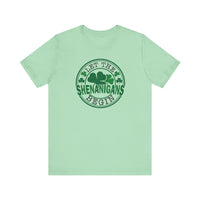 Let The Shenanigans Begin Tee features a green logo with four-leaf clovers, perfect for casual wear with ribbed knit collars and durable side seams.