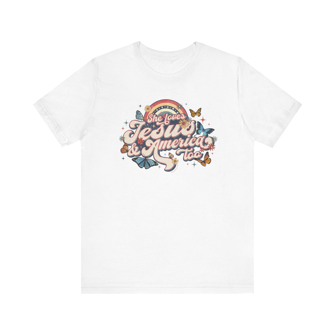 A white t-shirt featuring a graphic design of butterflies, flowers, and colorful text. Unisex jersey tee made of 100% Airlume combed cotton, with ribbed knit collars and tear-away label. She Loves Jesus and America Tee from Worlds Worst Tees.