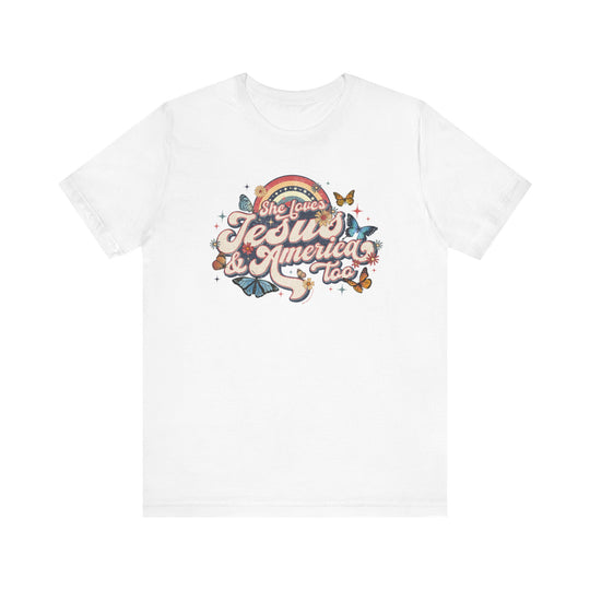 A white t-shirt featuring a graphic design of butterflies, flowers, and colorful text. Unisex jersey tee made of 100% Airlume combed cotton, with ribbed knit collars and tear-away label. She Loves Jesus and America Tee from Worlds Worst Tees.