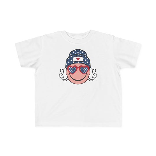 American Girl Toddler Tee featuring a cartoon face with sunglasses and a hat on a white shirt. Soft 100% combed ringspun cotton, tear-away label, classic fit. Available in sizes 2T to 5-6T.