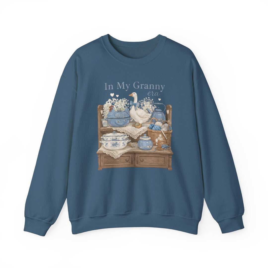 In My Granny Era Crew: A slate-blue sweatshirt featuring a vintage-style illustration of a tiered shelf with ceramic and knit items, hearts, and text.