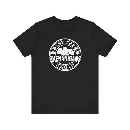 Let The Shenanigans Begin Tee, a black t-shirt featuring white text and clovers, offering a soft, retail fit with ribbed collars and taping for durability.