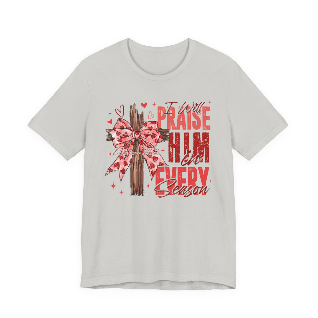 Light-gray tee featuring a wooden cross with a pink heart-patterned bow, text I Will Praise Him in Every Season, Psalm 146:2, ideal for faith-themed fashion.