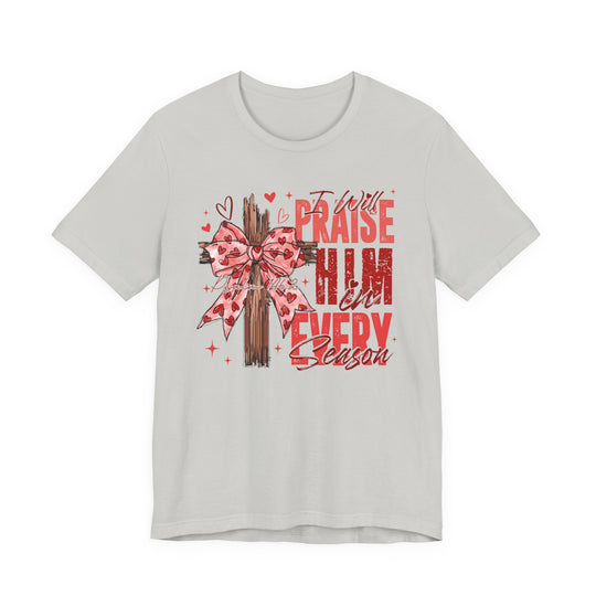 Light-gray tee featuring a wooden cross with a pink heart-patterned bow, text I Will Praise Him in Every Season, Psalm 146:2, ideal for faith-themed fashion.