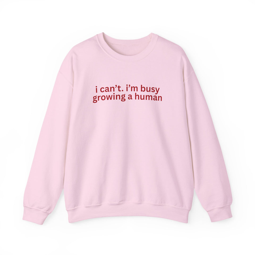 Light-pink crewneck sweatshirt with red text i can’t. i’m busy growing a human. on front, offering comfort with ethical, sustainable materials and durable construction.