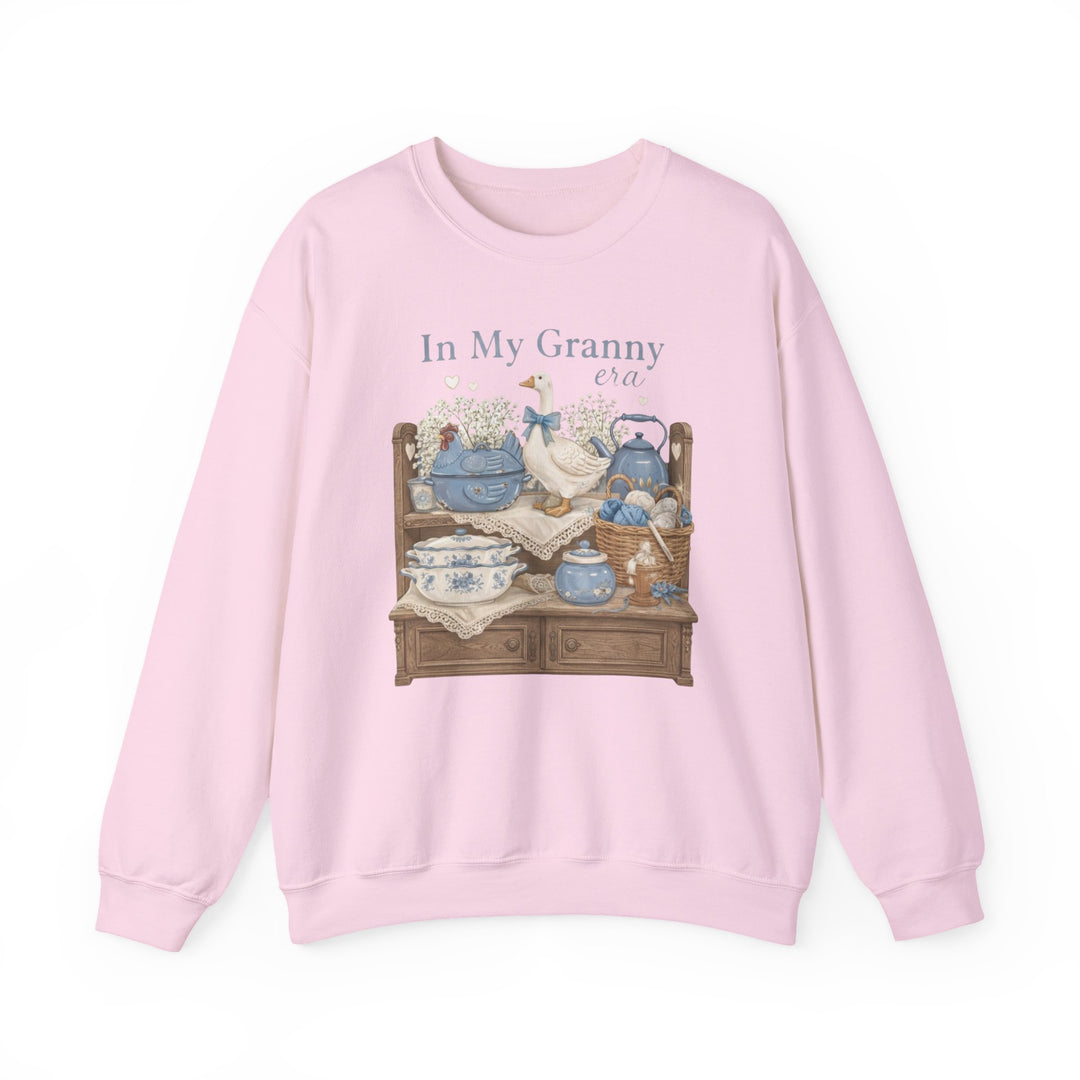 In My Granny Era Crew: Light-pink sweatshirt featuring a vintage hutch graphic with ceramics, a goose figurine, and yarn, capturing a cozy, nostalgic vibe.