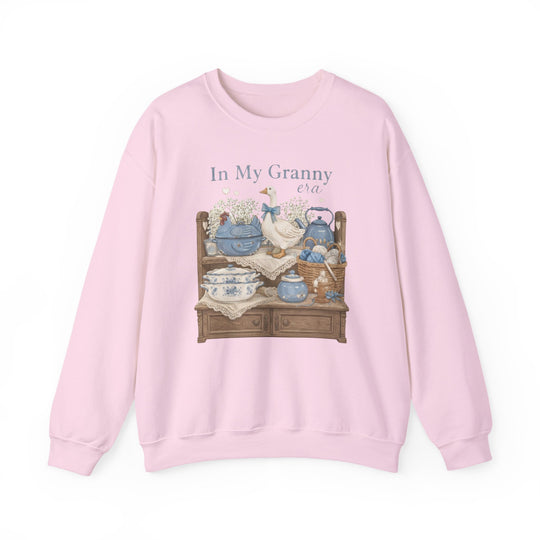 In My Granny Era Crew: Light-pink sweatshirt featuring a vintage hutch graphic with ceramics, a goose figurine, and yarn, capturing a cozy, nostalgic vibe.