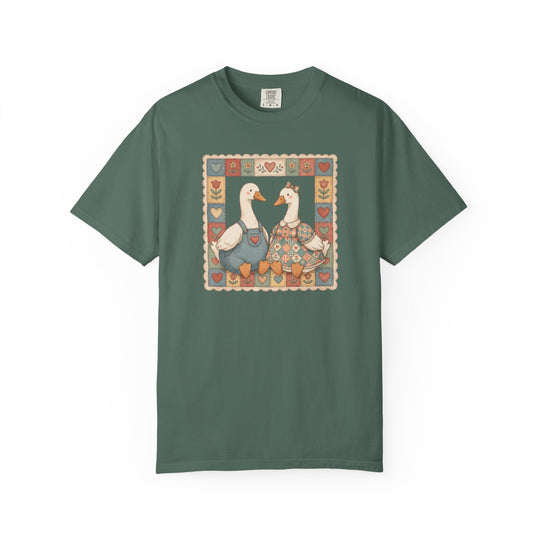 Thrifted Geese Tee featuring vintage-style geese in folk-art attire within a heart and flower quilted frame on a forest-green, short-sleeve shirt.