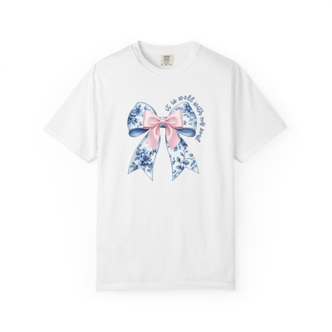 White T-shirt featuring a large decorative bow with a blue-and-white floral pattern and pink knot, encircled by the phrase “It is well with my soul”.