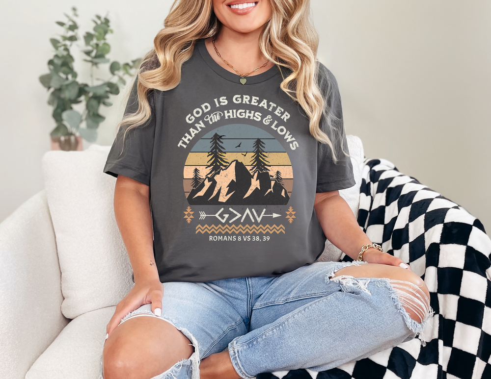 A woman wearing the God is Greater Tee sits casually on a couch, showcasing the shirt's comfortable fit and stylish design.