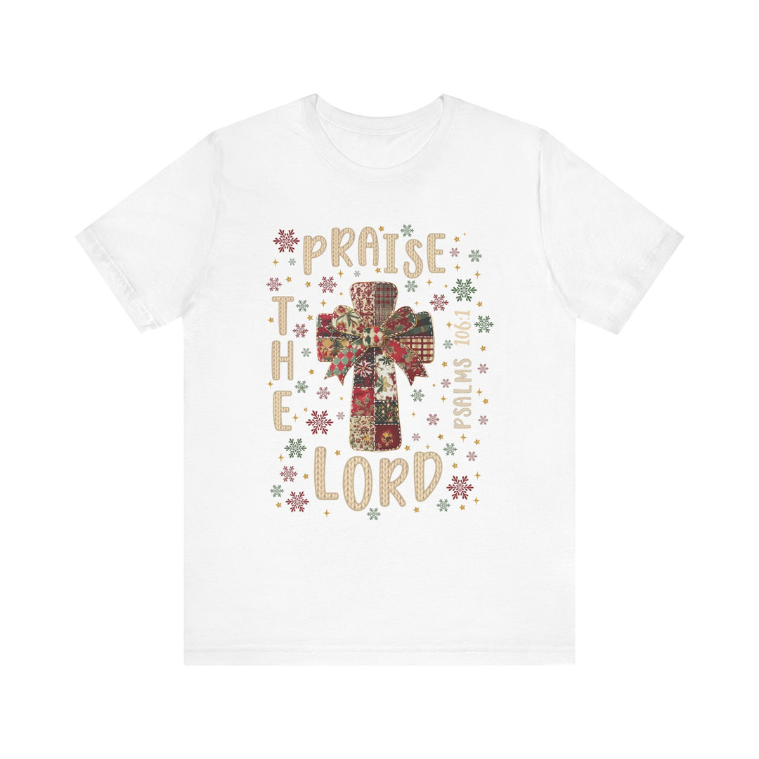 Praise the Lord Tee features a patchwork cross with a bow, snowflakes, and PRAISE THE LORD with Psalms 106:1 on a soft, unisex cotton shirt.