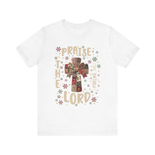 Praise the Lord Tee features a patchwork cross with a bow, snowflakes, and PRAISE THE LORD with Psalms 106:1 on a soft, unisex cotton shirt.