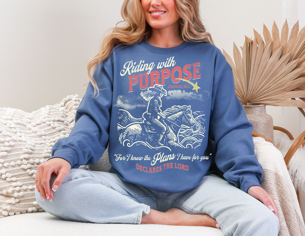 Woman wearing the Riding for a Purpose Crew sweatshirt, sitting on a couch, showcasing a comfortable, unisex fit with a graphic design.