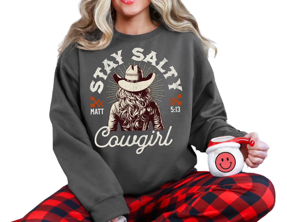 Woman in a Stay Salty Crew sweatshirt with a cowboy hat, sitting on a chair, holding a mug. The sweatshirt offers a comfortable fit and unique design.