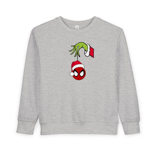 Spider Ball Christmas Toddler Crew: Light-gray sweatshirt featuring the Grinch's hand holding a Spider-Man ornament, perfect for festive, cozy wear.
