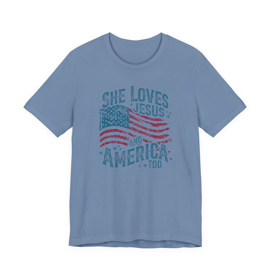 Light blue T-shirt with distressed American flag graphic and slogan She loves Jesus and America, too, highlighting patriotic faith.