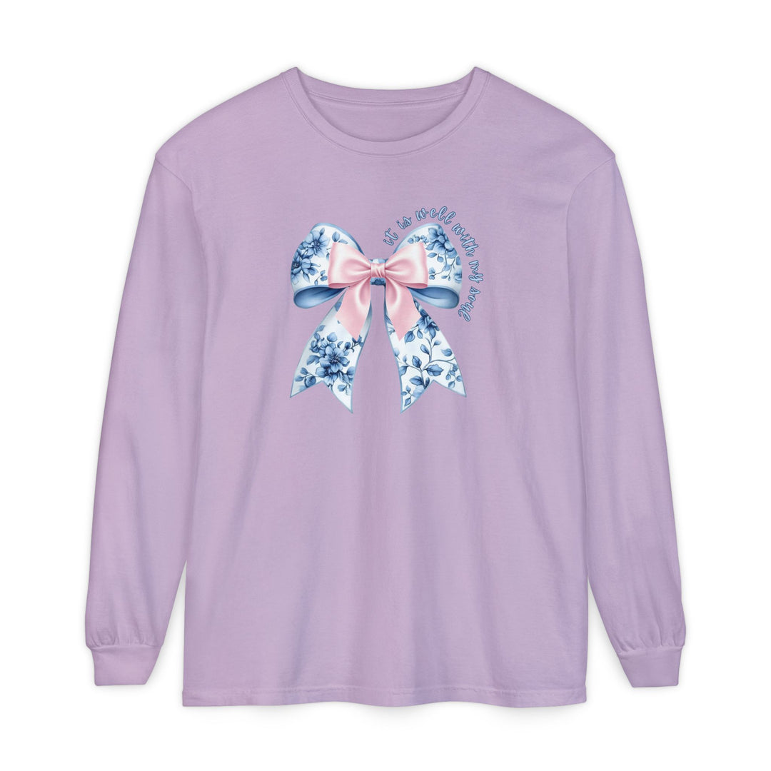 It is Well With My Soul Long Sleeve Tee featuring a lavender base, ornate bow graphic, and comforting phrase, crafted from soft, garment-dyed 100% cotton.