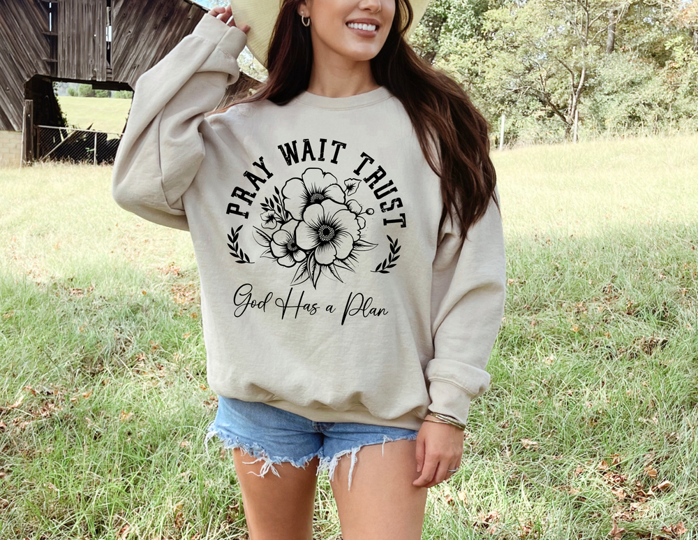 Woman wearing the Pray Wait Trust Crew sweatshirt, showcasing a black and white floral design, embodying casual comfort with a ribbed collar and loose fit.