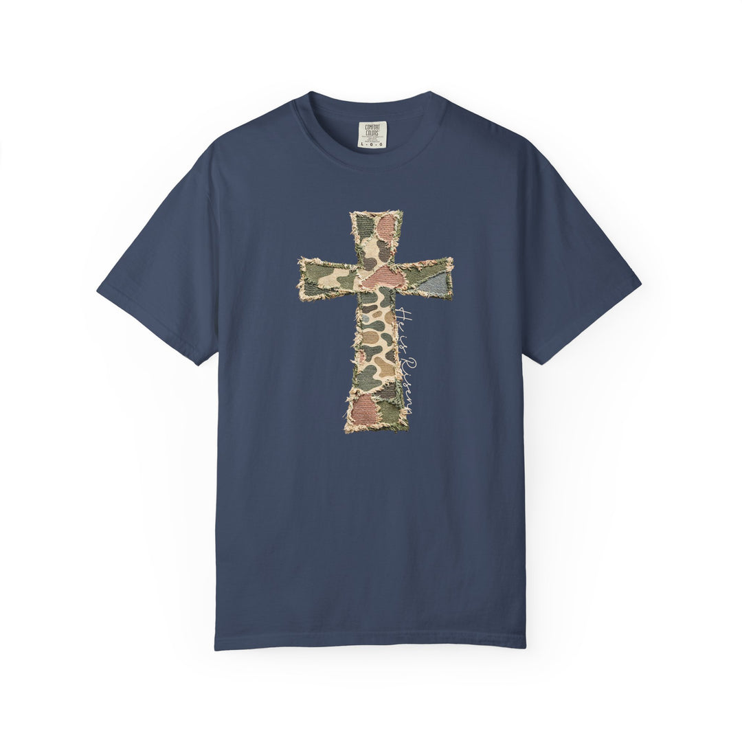 He is Risen Distressed Tee features a navy-blue design with a frayed-edge cross in camouflage and white script. Made from soft, durable Comfort Colors fabric.