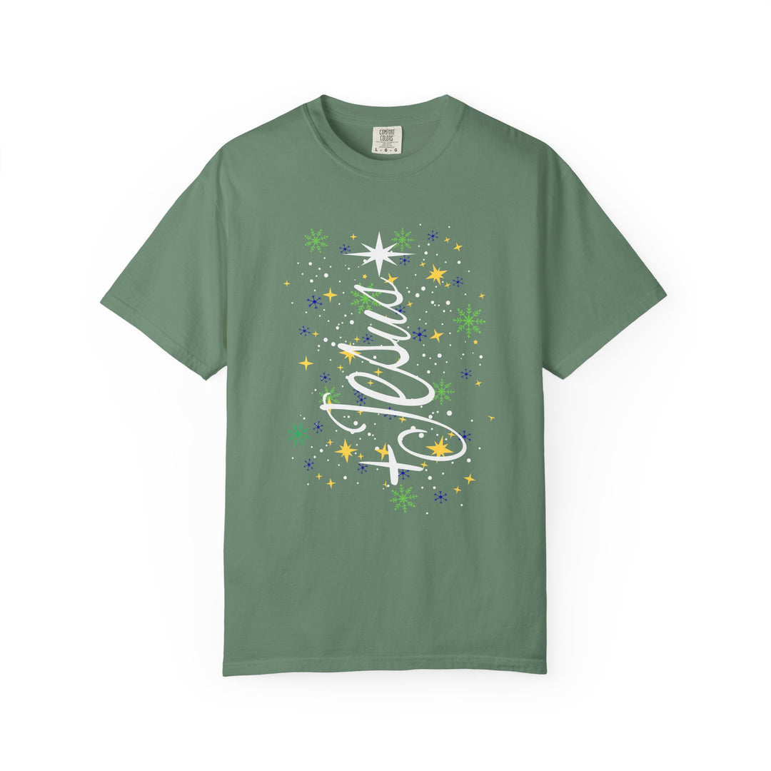 Sage-green Jesus Tree Tee featuring a festive snowflake and star graphic with a flowing cursive overlay, perfect for holiday-themed wear.