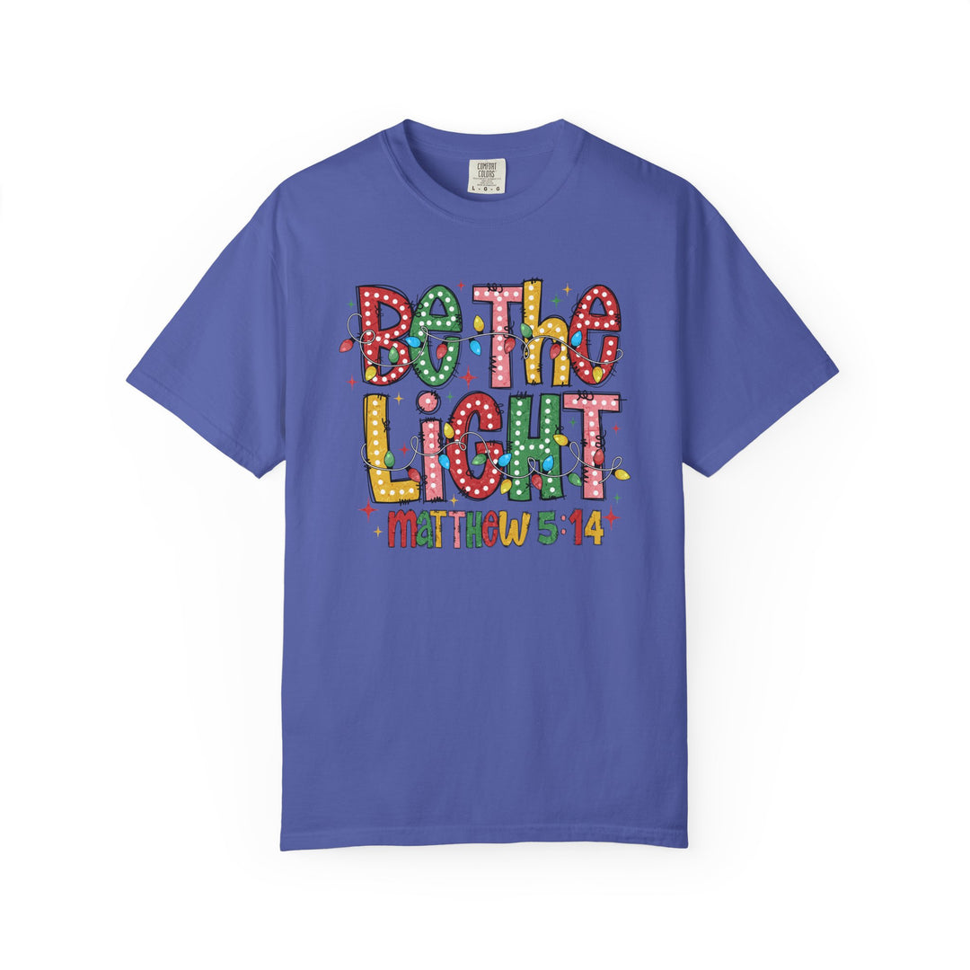 Be the Light Tee with vibrant lettering and light bulb accents, featuring 'Matthew 5:14' on a solid-blue short-sleeve shirt from Faith Family Designs.