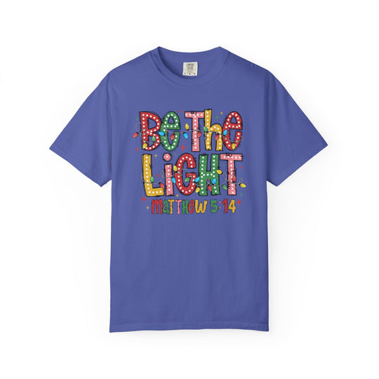 Be the Light Tee with vibrant lettering and light bulb accents, featuring 'Matthew 5:14' on a solid-blue short-sleeve shirt from Faith Family Designs.