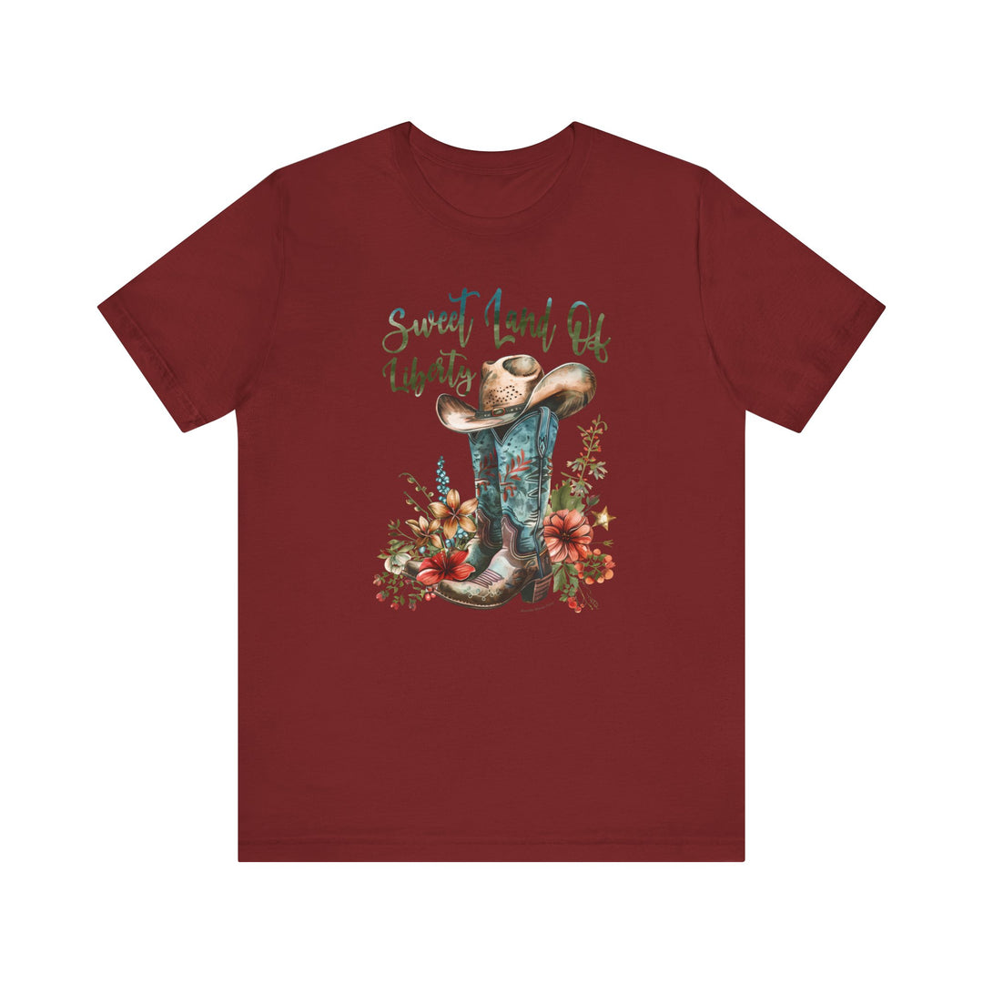 A red shirt featuring a cowboy hat and flowers, embodying a classic Americana vibe. Unisex jersey tee made of 100% Airlume combed cotton, with ribbed knit collars and taping for durability. Sweet Land of Liberty Tee from Worlds Worst Tees.