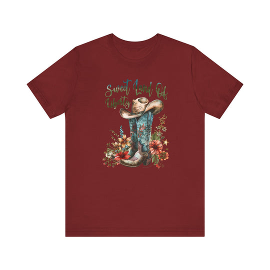 A red shirt featuring a cowboy hat and flowers, embodying a classic Americana vibe. Unisex jersey tee made of 100% Airlume combed cotton, with ribbed knit collars and taping for durability. Sweet Land of Liberty Tee from Worlds Worst Tees.