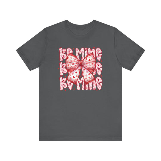 Be Mine Tee featuring a playful pink ribbon and Be Mine text with heart accents on a dark charcoal-gray T-shirt, perfect for Valentine's Day.