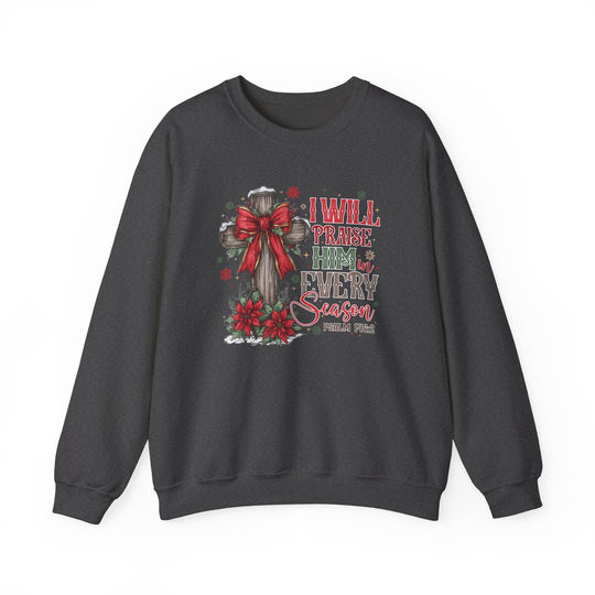Dark-charcoal crewneck sweatshirt with wooden cross, red bow, poinsettias, and text “Praise Him in Every Season,” reflecting a Christian Christmas theme.