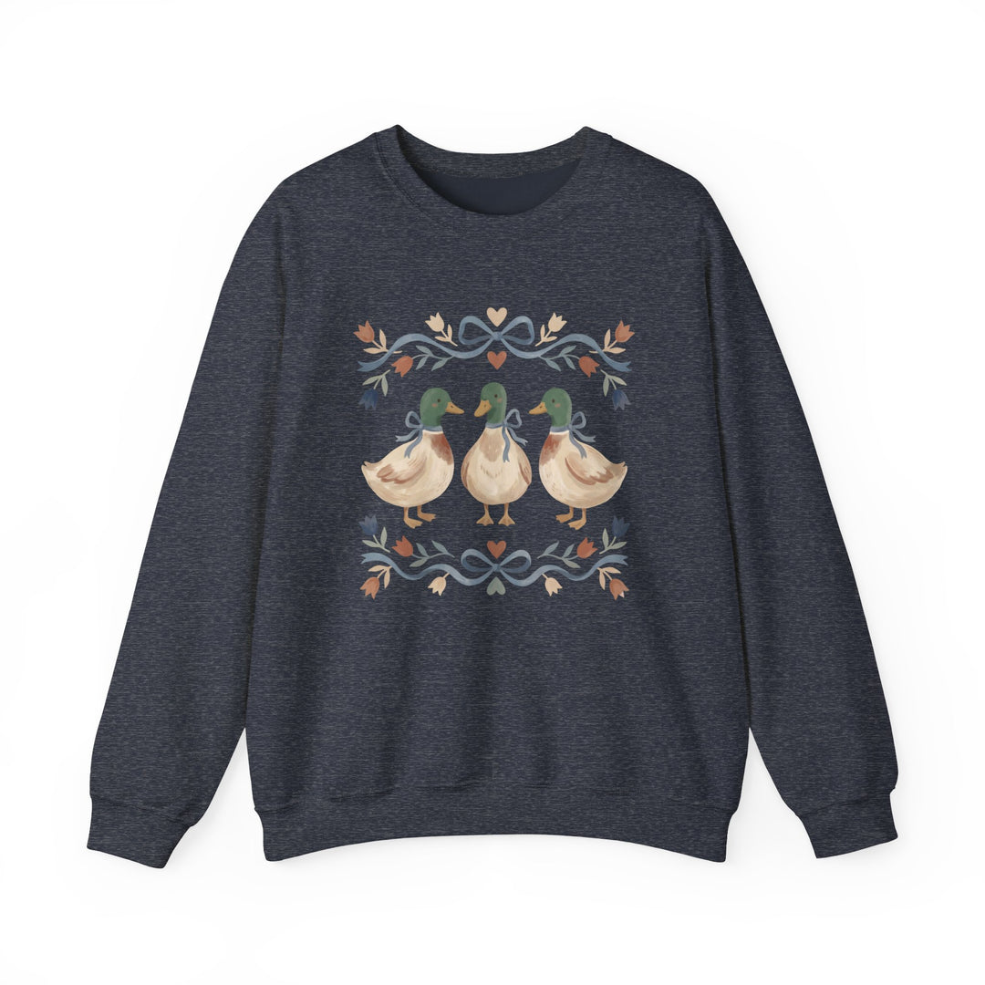 Cottagecore Crew: Dark-heather navy sweatshirt with folk-art graphic of three mallard ducks in bows, framed by stylized floral garland. Cozy unisex fit.