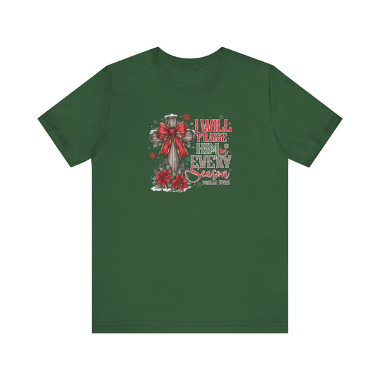 Praise Him in Every Season Tee: Forest-green T-shirt featuring a wooden cross with a red bow, poinsettias, snowflakes, and Psalm 146:2, promoting faith in every season.